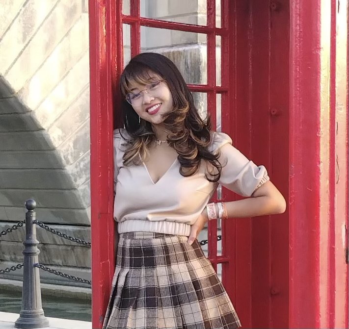 a woman is posing in front of a red telephone booth.