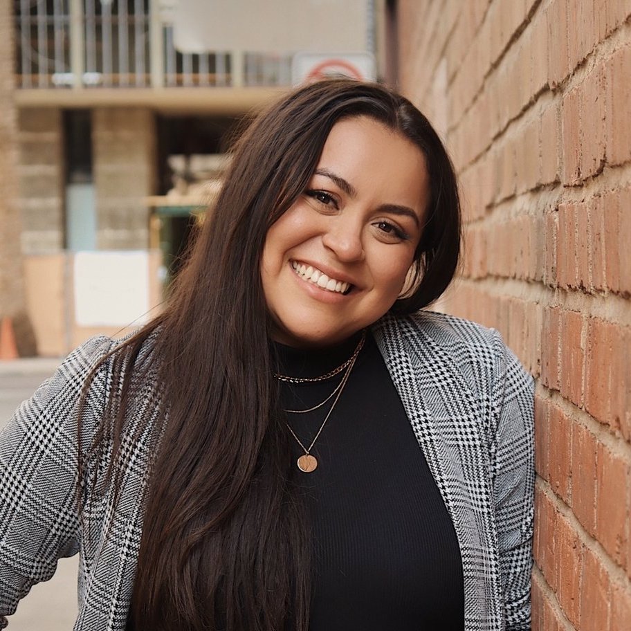 a smiling woman leaning against a brick wall.