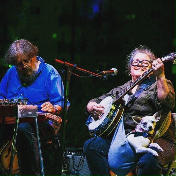 a man and woman playing banjo on stage with a dog.