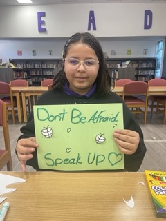 a girl holding up a sign that says don't be afraid to speak up.