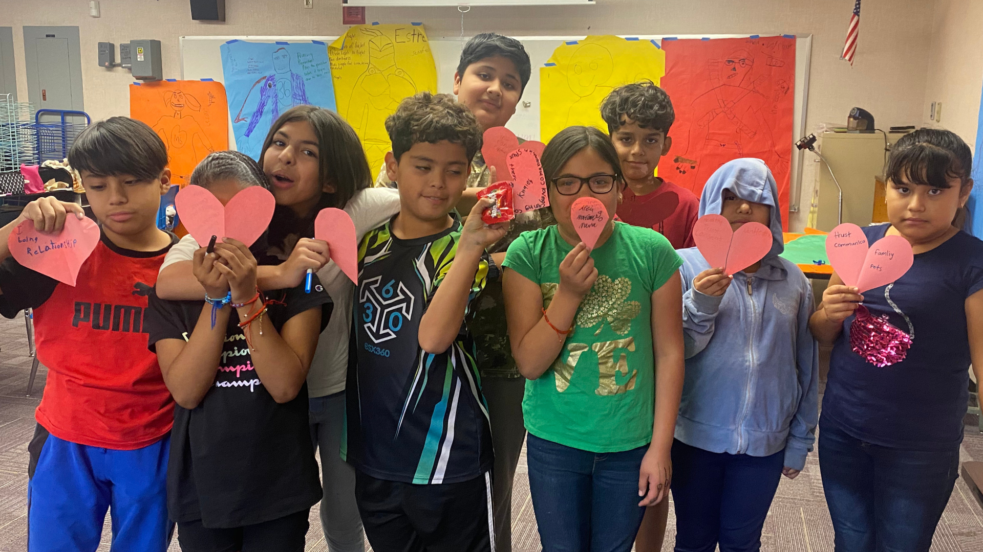 a group of kids holding up paper hearts in a classroom.