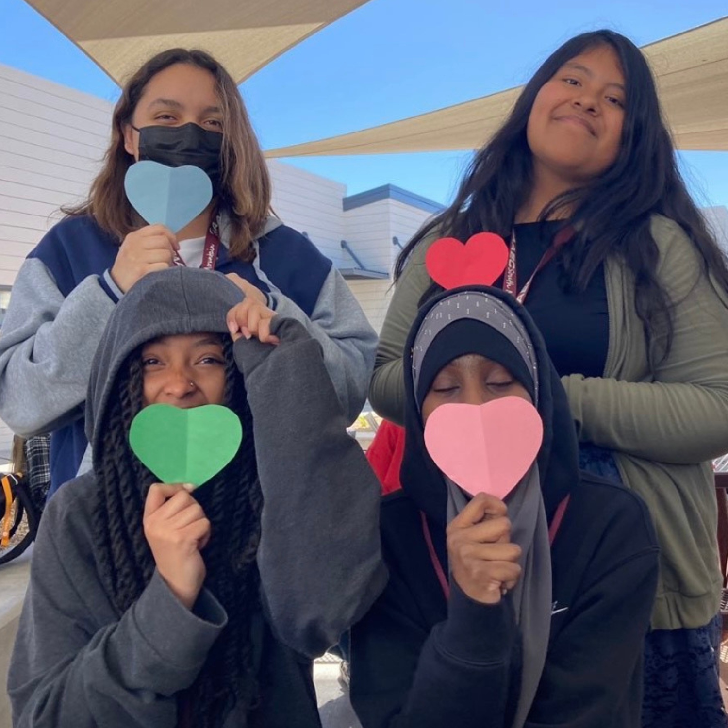 four girls holding up heart shaped paper cut outs.